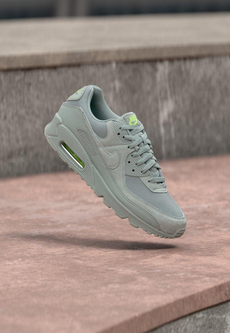 Chaussure de sport grise en mesh et daim, dotée d'une unité d'air translucide, d'accents néon et d'une semelle texturée.