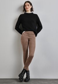 Leggings in suede marrone abbinati a un maglione nero. I leggings hanno una texture liscia e l'outfit comprende stivaletti neri alla caviglia.