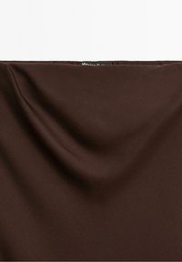 Tissu marron foncé à la texture lisse avec des plis subtils, arborant une petite étiquette noire en haut au centre portant l'inscription « Massimo Dutti ».