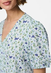 Vestido de estampado floral en azul claro, con mangas abullonadas y escote en V profundo. La tela tiene un acabado texturizado con flores verdes y azules.