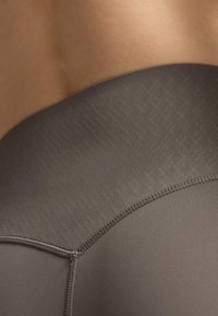 Dunkelgraue Sportleggings mit glatter Textur, niedrig sitzendem Bund und dezenter Musterung, versehen mit präzisen Nahtdetails.