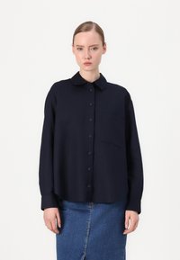 Marineblauw longsleeve shirt met een knoopsluiting aan de voorkant, een kraag en een enkel borstzakje, gecombineerd met een blauwe spijkerrok. Soepele stofstructuur.