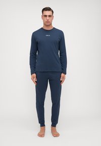 Cămașă albastră închis cu mânecă lungă și pantaloni asortați, din material moale, cu un mic logo pe piept, cu manșete și talie elastice.