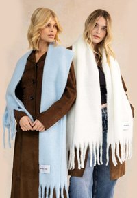 Deux femmes portent de longues écharpes douces : l'une en bleu clair et l'autre en blanc. Les deux ont des bords à franges et comportent des étiquettes de marque.