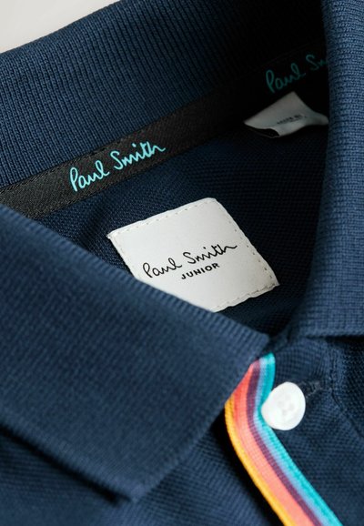 Tengerészkék póló, texturált anyagból készült, három gombos elejével és "Paul Smith JUNIOR" feliratos címkével. Több színű díszítések a galléron.