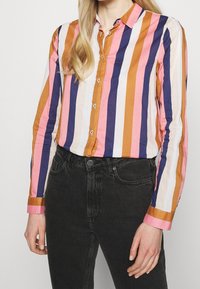 Knapp-up randig skjorta med vertikala ränder i färgerna: orange, marinblå, rosa och vit. Tillverkad av lätt bomull, med långa ärmar.