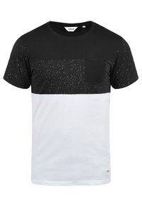 Camiseta en blanco y negro con una textura moteada, cuello redondo, mangas cortas y un pequeño bolsillo en el pecho. Material de algodón suave.