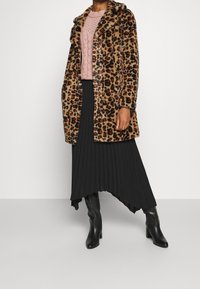 Leopardmönstrad faux fur-kappa med långa ärmar och krage, kombinerad med en ljusrosa stickad tröja och en svart plisserad kjol, kompletterad med svarta klackboots.