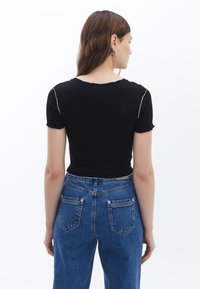 Schwarzes, verkürztes T-Shirt mit kurzen Ärmeln und rohen Kanten, kombiniert mit hochtaillierten blauen Jeans aus Denim, die über Rücken taschen und sichtbare Nähte verfügen.