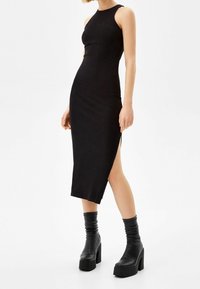 Robe midi noire côtelée avec col haut et fente latérale, associée à des bottes noires à plateforme montant jusqu'aux genoux. Texture lisse, coupe ajustée.