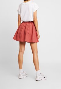 Gonna a skater rossa in lino con vita arricciata e una forma leggermente svasata, abbinata a una maglietta bianca con maniche arrotolate e sneakers bianche.