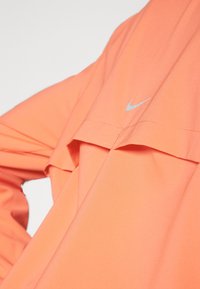 T-shirt Nike en corail vif, présentant un design en couches avec une coupe ample, des manches courtes et un logo argenté subtil sur la poitrine.