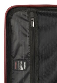 Red luggage interior with black mesh pockets, zipper closures, and a label. Textured fabric and horizontal lines visible.