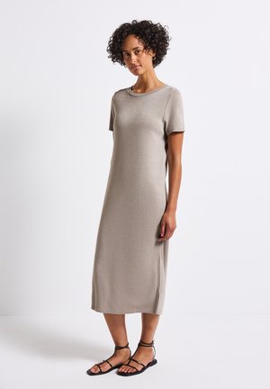Knee-length, fitted dress in light taupe with a subtle shimmer. Short sleeves, round neck, and side slits. Paired with black sandals.