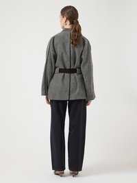 Chaqueta gris con estampado y cinturón negro, combinada con jeans oscuros de pierna ancha. Mangas largas y cuello alto completan el conjunto.