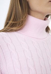 Světle růžový rolák se strukturou z žebrovaného materiálu a vzorem kabelkového pletení. Výstřih je vysoký a přiléhavý. Měkký pletený materiál.