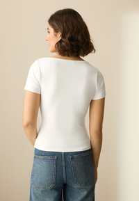 Haut blanc à manches courtes avec un col rond, une coupe ajustée et une texture lisse, associé à un jean denim bleu taille haute.