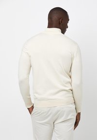 Hellbeige Pullover mit hohem Kragen, gerippten Bündchen und taillierter Passform. Hergestellt aus weichem, glattem Stoff. Geeignet für die Freizeit.