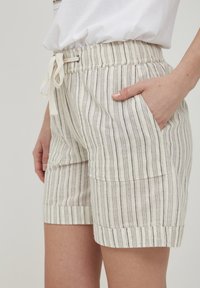 Shorts en lin avec des rayures verticales beiges et noires, affichant une taille élastique avec cordon de serrage, des poches latérales et des ourlets retournés.
