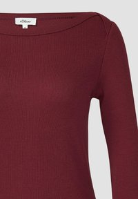 Bordowa bluzka z długim rękawem wykonana z prążkowanej tkaniny, z dekoltem typu łódka i dopasowanym krojem. Posiada subtelne detale przeszyć wzdłuż kołnierza.