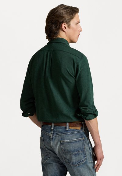 Grønn langermet skjorte med rullede ermer, knappe mansjetter og krage; brukt med blå jeans som viser lapper og lomme detaljer.