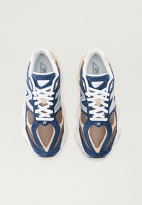 Athletic sneakers with a blue and beige mesh upper, white laces, cushioned sole, and prominent "N" logo on the side.