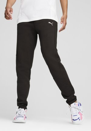 Pantalones de chándal negros con un diseño ajustado, que presentan un logo de Puma blanco, paneles laterales texturizados y puños elásticos. Combinados con zapatillas deportivas coloridas.