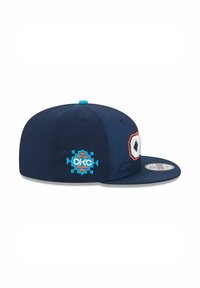Casquette bleu marine avec une visière plate, un logo brodé en orange et blanc, et des accents décoratifs turquoise sur le côté et le bouton supérieur.