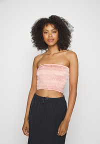 Top curto strapless rosa claro com textura franzida; modelo usa com uma saia preta com cordão. Material suave e design ajustado.
