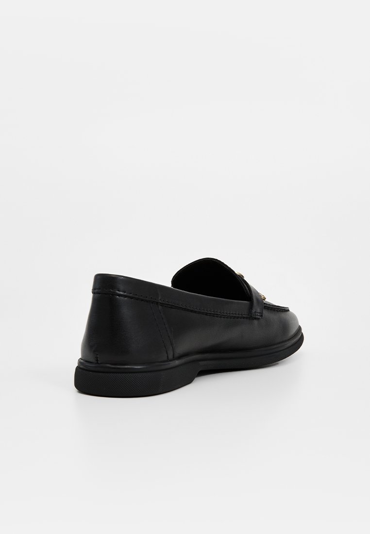 Mocassin en cuir noir avec un talon bas, une toe arrondie et un détail en boucle métallique décorative, présenté de l'angle arrière sur un fond blanc.
