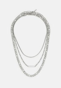 Collier en chaîne argenté à plusieurs couches présentant des épaisseurs et des designs variés, y compris une chaîne à maillons plats et une chaîne en chevrons lisse.