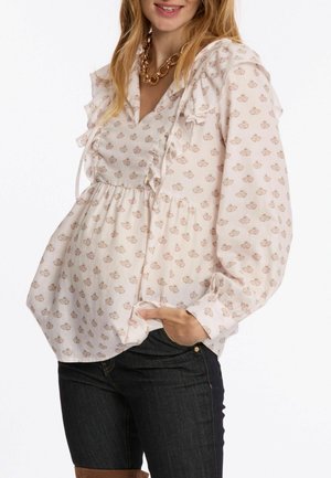 Lichtroze blouse met geschulpte schouders, V-hals en bloemenpatroon. Vloeiende stof met een geraffineerde taille, gecombineerd met donkere jeans.