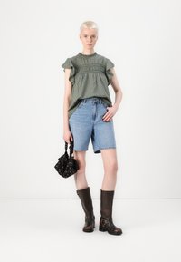 Grøn mønstret top med flæser på ærmerne, blå denim shorts, sort blomsterhandtaske og brune støvler til knæene. Enkel og afslappet sæt.