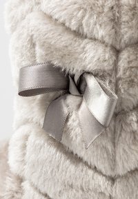 Tissu en peluche gris pâle avec une texture douce et duveteuse, présentant des lignes matelassées cousues et un nœud en satin gris en accent sur le côté.