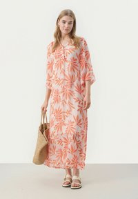 Lång, genomskinlig klänning med ett abstrakt blommönster i orange på en ljusrosa bakgrund. Har en V-ringning och vida ärmar. Bärs med sandaler.