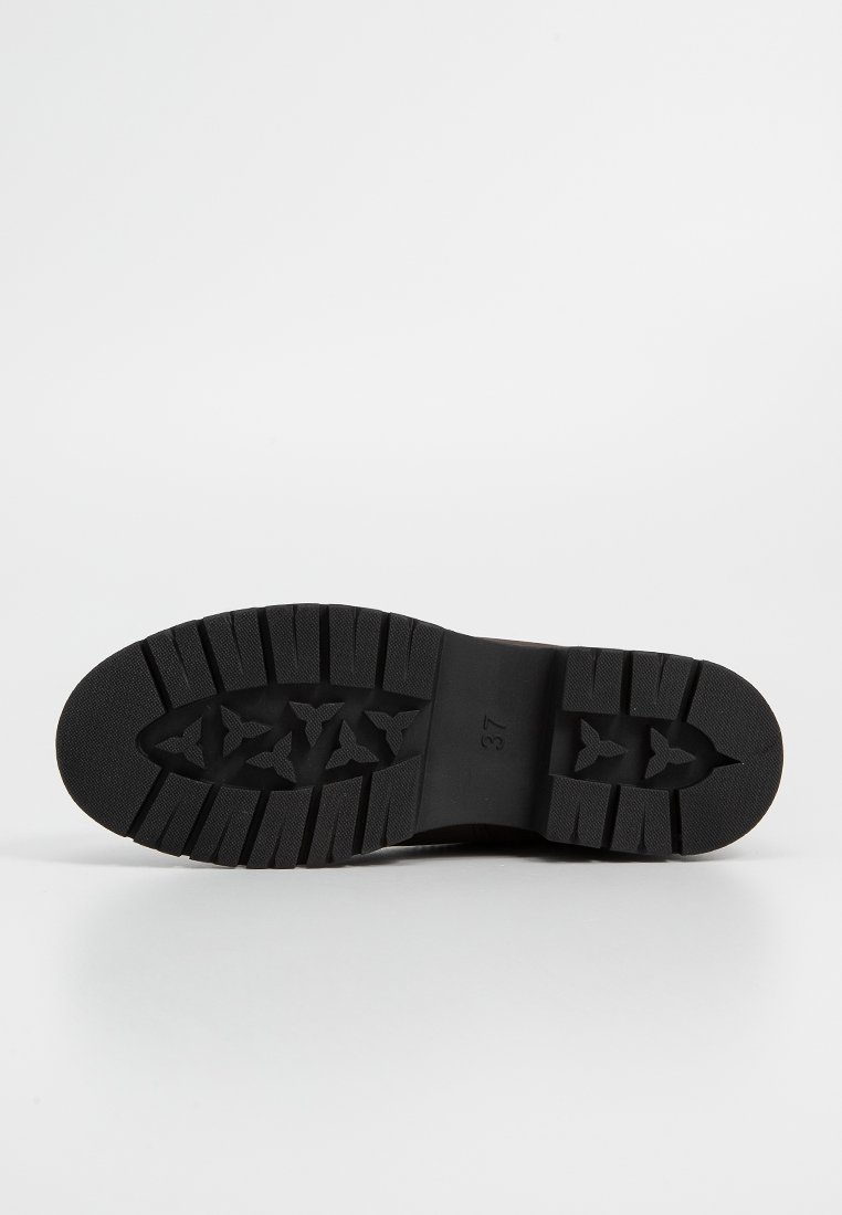 Suela de zapato de goma negra con surcos profundos y patrones de tracción. Presenta una punta redondeada y una talla marcada "37" para identificación.