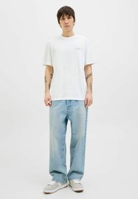 Tricou alb din bumbac, cu mâneci scurte, croială lejeră și un logo mic pe piept. Asortat cu blugi lejeri din denim albastru deschis și adidași gri.