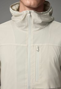 Light beige zip-up jacket with a high collar, textured fabric, and a chest pocket with a vertical zipper. Minimalist design.