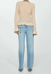 Jasno-beżowy sweter dzianinowy z rozszerzonymi rękawami i falbaniastym dołem, zestawiony z jasnoniebieskimi dżinsami o prostym kroju z postrzępionym dołem i łańcuszkowym dodatkiem.