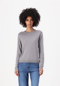 Grå långärmad tröja i mjukt material, med rund halsringning och ribbad nederkant. I kombination med blå denimjeans.