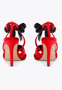 Czerwone zamszowe sandały na wysokim obcasie z czarnymi materiałowymi kokardami i koralikowymi zdobieniami, z krzyżującymi się paskami i smukłym obcasem szpilką.