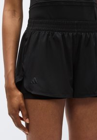 Μαύρο αθλητικό σορτς με ελαστική μέση, στρωματοποιημένο σχέδιο και ασημί λογότυπο στο πλάι, με ελαφρύ, λείο ύφασμα.