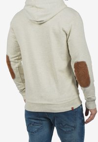 Felpa con cappuccio in tessuto beige chiaro con toppe sui gomiti in marrone testurizzato. Presenta polsini e orlo a costine, e un design dal taglio casual.