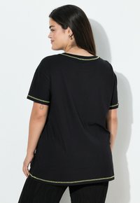 Sort t-shirt med korte ærmer, rund halsudskæring og kontrastfarvet grøn syning langs kraven og ærmerne. Blødt, letvægts stof.