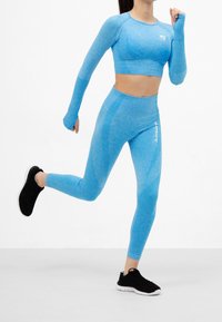 Ljusblå idrottcropped topp och matchande leggings med texturerade mönster, tillsammans med svarta träningsskor, i en aktionställning.