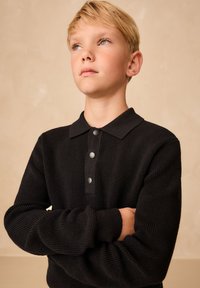 Polo en maille noire avec un motif texturé, doté d'un col et de trois boutons en métal. Comprend des manches longues avec des poignets côtelés.