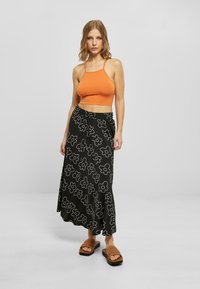 Orange cropped tank top paired with a black floral-patterned maxi skirt. Model wears brown woven sandals. Plain grey background.