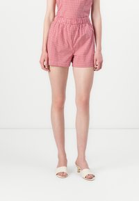 Pantalones cortos de cuadros rojo y blanco con cintura elástica, de corte relajado. Combinados con zapatos de tacón abiertos en beige que presentan un detalle dorado.