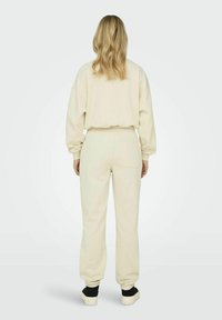 Beige Loungewear-Set mit einem lässig geschnittenen Sweatshirt mit Rundhalsausschnitt und einer Jogginghose mit Bundfalten und einer Gesäßtasche. Weicher Stoff.