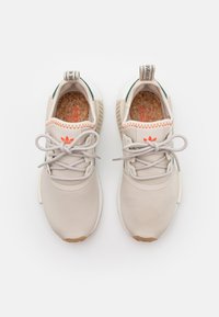 Beige sportskor med överdel i texturerat tyg, orange sömmar, gröna detaljer och en vadderad korksula. Gummisula för bra grepp.